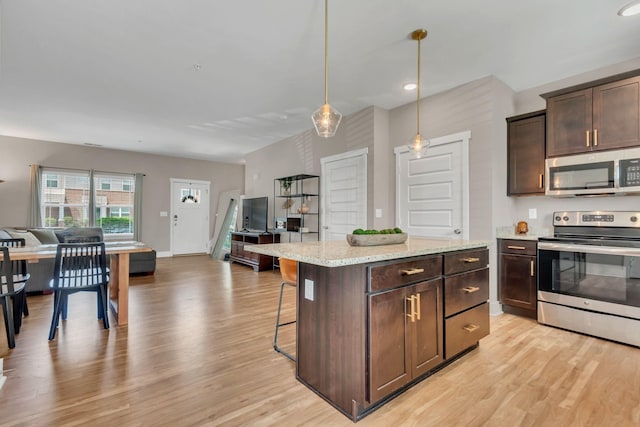 kitchen with appliances with stainless steel finishes, open floor plan, light wood-type flooring, dark brown cabinets, and a kitchen bar