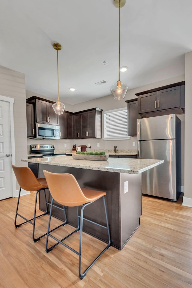 kitchen with appliances with stainless steel finishes, dark brown cabinetry, light wood-type flooring, a kitchen island, and recessed lighting