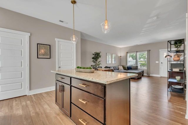 kitchen with light wood finished floors, baseboards, light stone counters, and hanging light fixtures