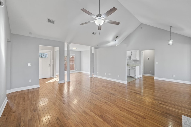 unfurnished living room with decorative columns, ceiling fan, light wood-style floors, baseboards, and high vaulted ceiling
