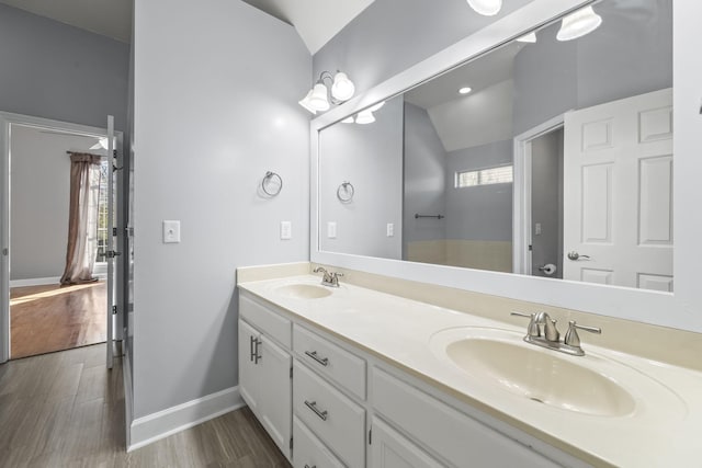 bathroom featuring vaulted ceiling, wood finished floors, double vanity, and baseboards
