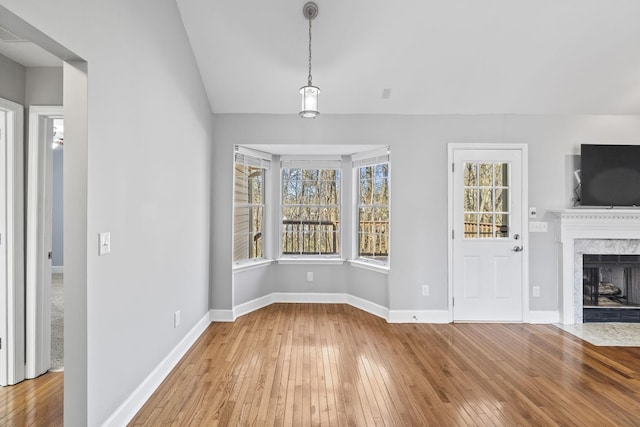 unfurnished living room with wood-type flooring, a high end fireplace, baseboards, and lofted ceiling