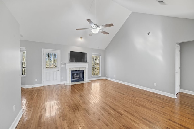 unfurnished living room featuring a ceiling fan, high vaulted ceiling, light wood finished floors, healthy amount of natural light, and a high end fireplace