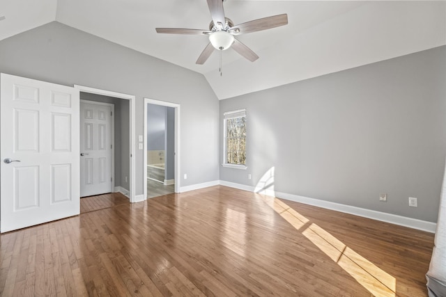 unfurnished bedroom with vaulted ceiling, wood finished floors, baseboards, ensuite bathroom, and ceiling fan