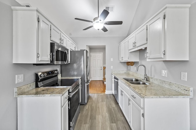 kitchen featuring stainless steel appliances, a sink, ceiling fan, light wood finished floors, and white cabinetry