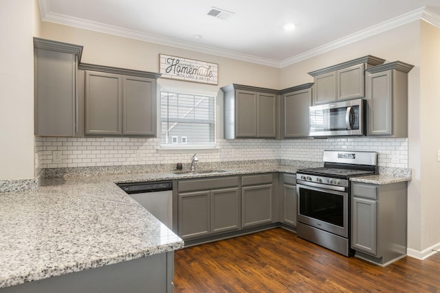 kitchen with stainless steel appliances, a sink, gray cabinetry, dark wood finished floors, and decorative backsplash