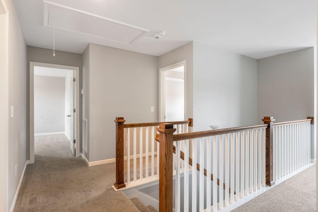 hall featuring attic access, an upstairs landing, carpet flooring, and baseboards
