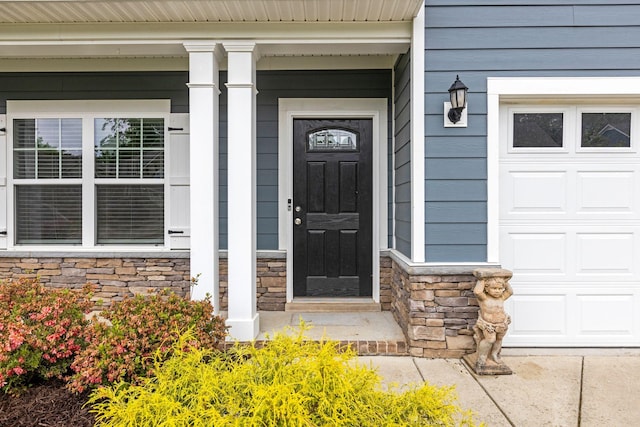 view of exterior entry featuring stone siding, covered porch, and an attached garage