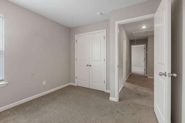 unfurnished bedroom featuring attic access, light colored carpet, baseboards, and a closet