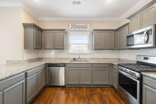 kitchen featuring stainless steel appliances, a sink, gray cabinets, ornamental molding, and decorative backsplash