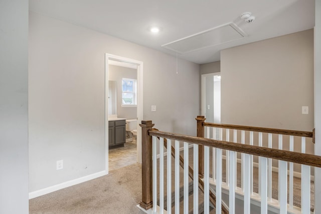 corridor featuring attic access, an upstairs landing, light carpet, and baseboards