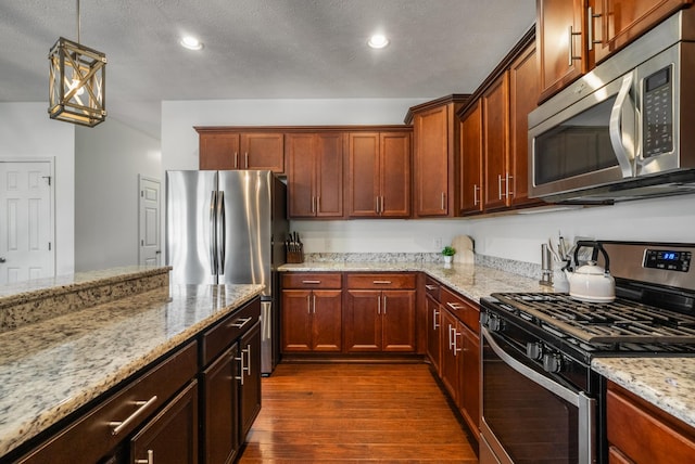 kitchen with appliances with stainless steel finishes, dark wood-style floors, light stone counters, recessed lighting, and hanging light fixtures