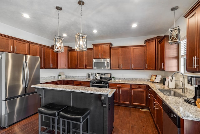 kitchen featuring appliances with stainless steel finishes, a sink, dark wood finished floors, a breakfast bar, and light stone countertops