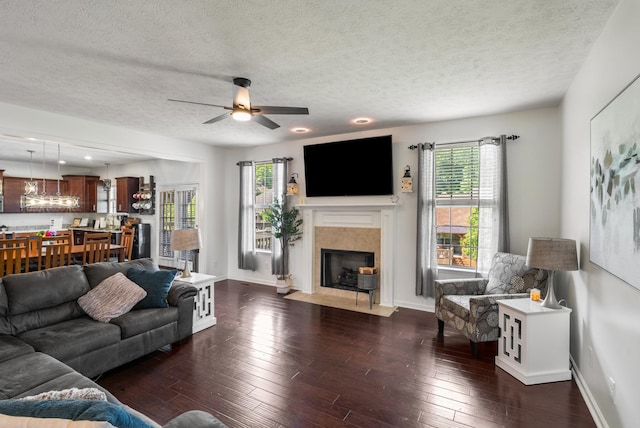 living area featuring a premium fireplace, a textured ceiling, dark wood-style flooring, baseboards, and a ceiling fan