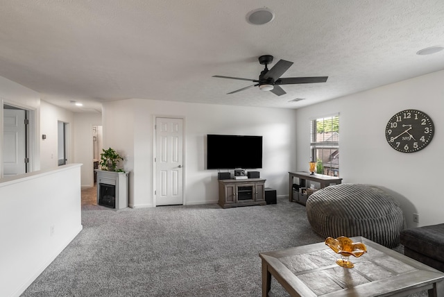 carpeted living area with a ceiling fan, a fireplace, baseboards, and a textured ceiling