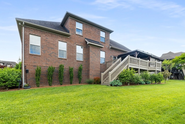 rear view of house with brick siding, stairs, a yard, a deck, and a shingled roof