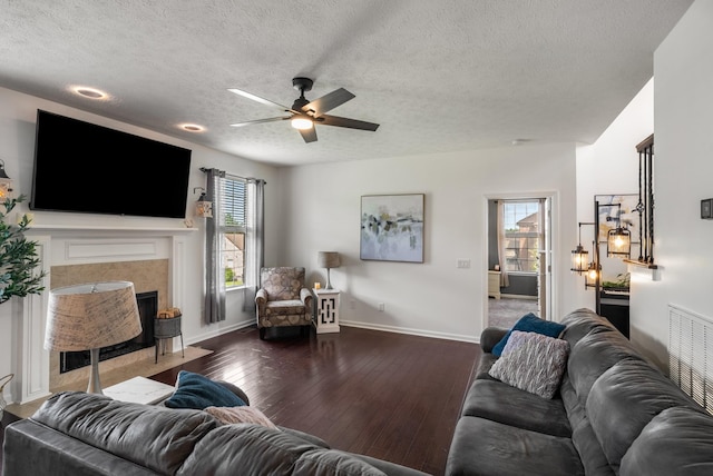living room featuring a ceiling fan, a textured ceiling, hardwood / wood-style flooring, baseboards, and a tiled fireplace