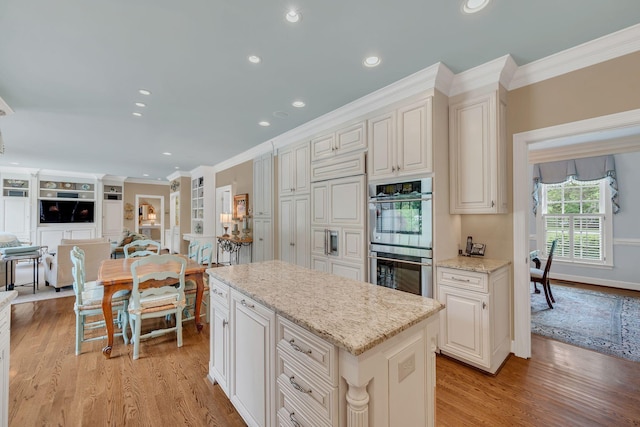 kitchen with stainless steel double oven, crown molding, light wood-style floors, a kitchen island, and open floor plan