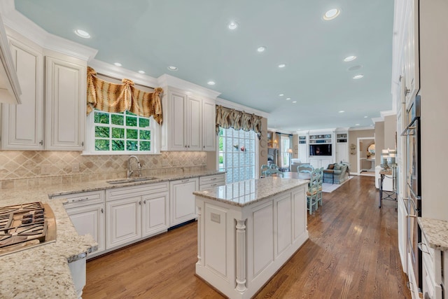 kitchen with a sink, a center island, open floor plan, crown molding, and stainless steel gas stovetop