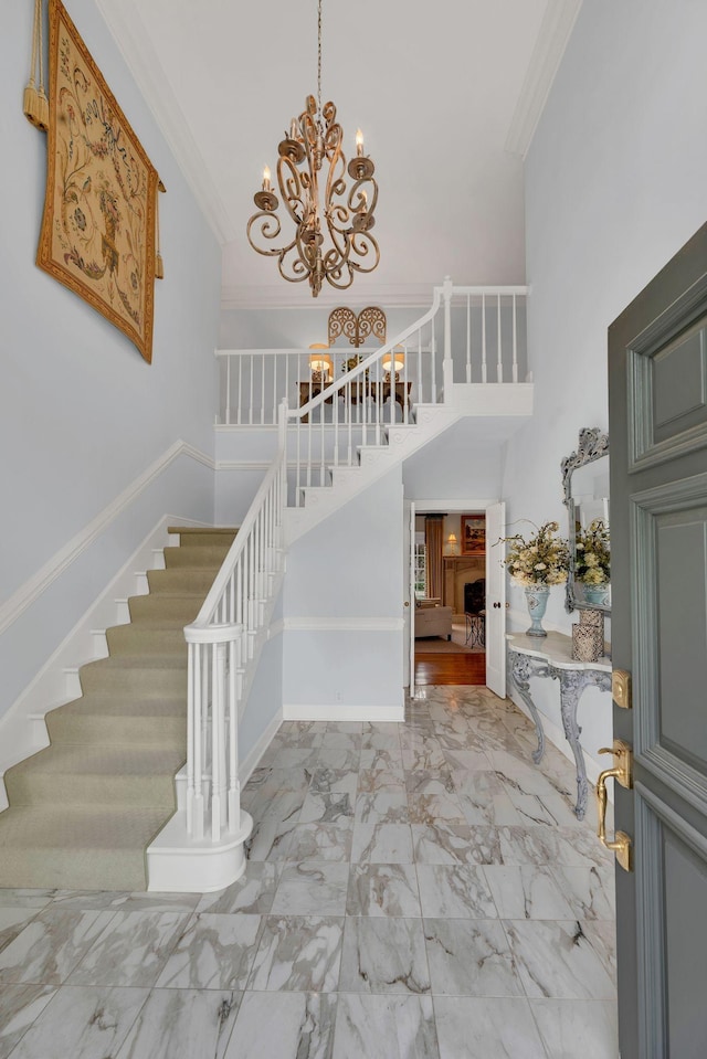 foyer entrance with stairway, a chandelier, crown molding, marble finish flooring, and a towering ceiling