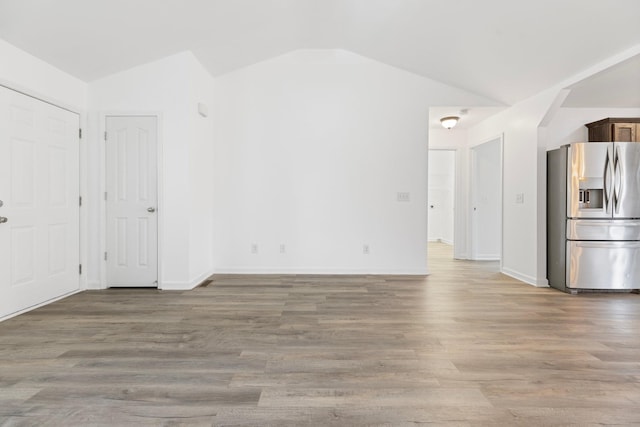 unfurnished living room featuring vaulted ceiling, wood finished floors, and baseboards
