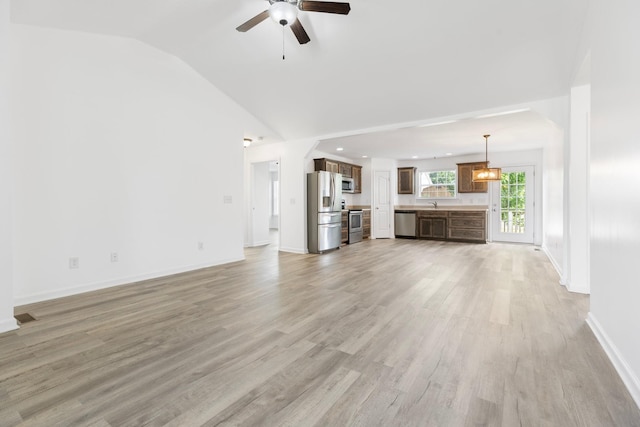 unfurnished living room featuring lofted ceiling, a ceiling fan, light wood-style floors, baseboards, and a sink