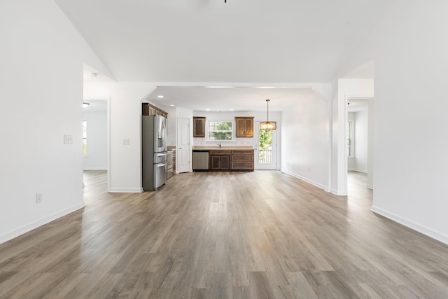 unfurnished living room with light wood finished floors, a sink, baseboards, and vaulted ceiling