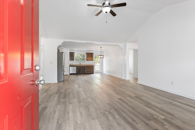 unfurnished living room with a ceiling fan, light wood-style floors, baseboards, lofted ceiling, and arched walkways