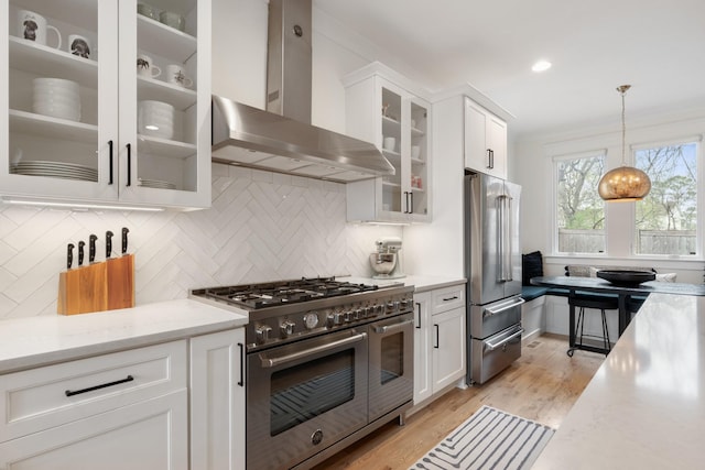 kitchen featuring high quality appliances, wall chimney exhaust hood, light countertops, white cabinets, and light wood-style flooring
