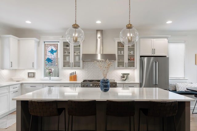 kitchen with appliances with stainless steel finishes, wall chimney range hood, a kitchen island, decorative backsplash, and recessed lighting