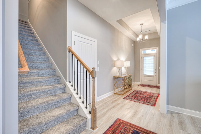foyer entrance with stairs, wood finished floors, a raised ceiling, a chandelier, and baseboards