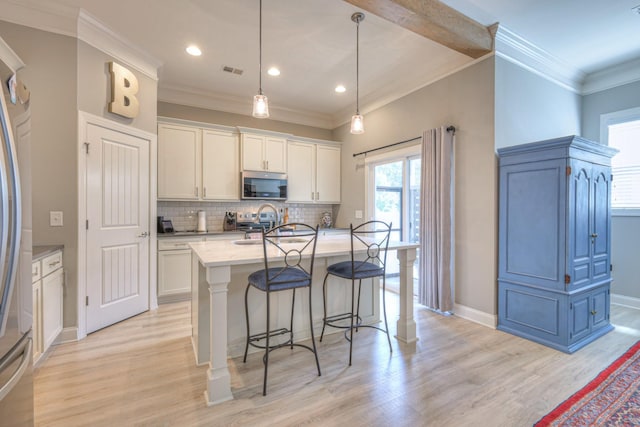 kitchen with stainless steel microwave, decorative backsplash, a breakfast bar, light wood-style flooring, and crown molding