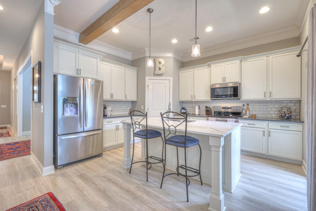 kitchen with stainless steel appliances, crown molding, white cabinets, backsplash, and a kitchen bar