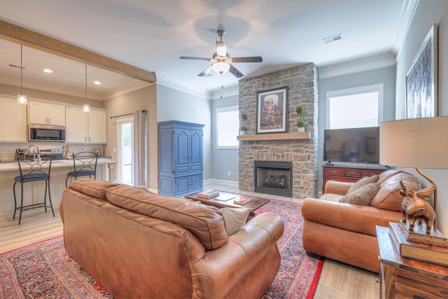 living area featuring a ceiling fan, light wood finished floors, a stone fireplace, recessed lighting, and crown molding