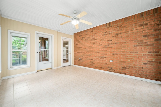 unfurnished room featuring brick wall, baseboards, a ceiling fan, and light floors