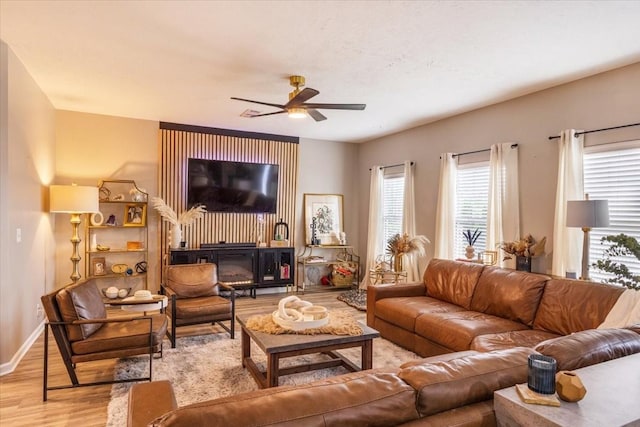 living area featuring light wood-type flooring, a ceiling fan, plenty of natural light, and baseboards