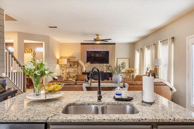 kitchen featuring a sink, open floor plan, a ceiling fan, and light stone counters