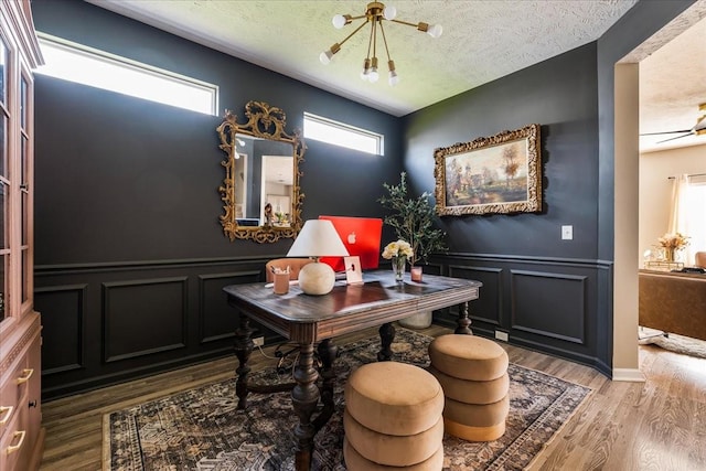 office space featuring a decorative wall, healthy amount of natural light, wood finished floors, a wainscoted wall, and a textured ceiling