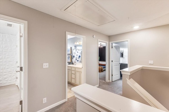 hallway featuring attic access, carpet floors, and baseboards