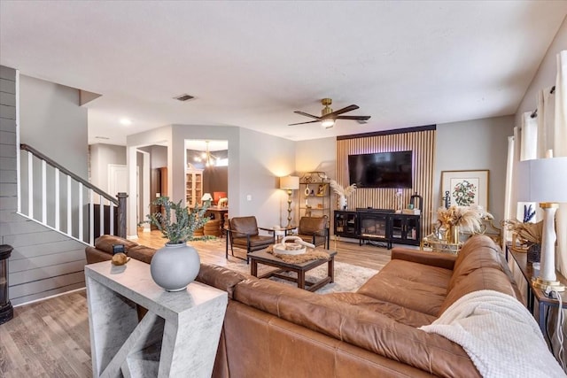 living area with light wood-type flooring, stairs, a ceiling fan, and a chandelier