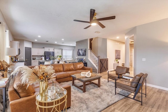 living room featuring light wood-style floors, stairs, ceiling fan, baseboards, and recessed lighting