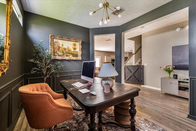 office space with a textured ceiling, a chandelier, wood finished floors, a wainscoted wall, and a decorative wall