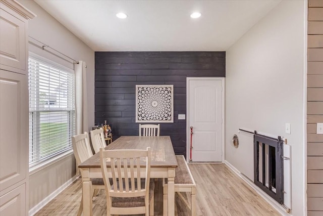 dining space featuring light wood finished floors, wood walls, recessed lighting, and baseboards