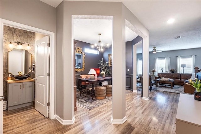 corridor with light wood-style flooring, baseboards, and a chandelier