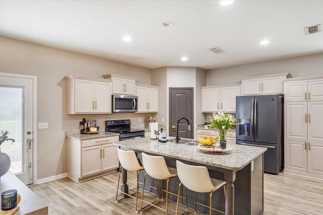 kitchen featuring stainless steel appliances, light wood finished floors, white cabinets, a center island with sink, and a sink