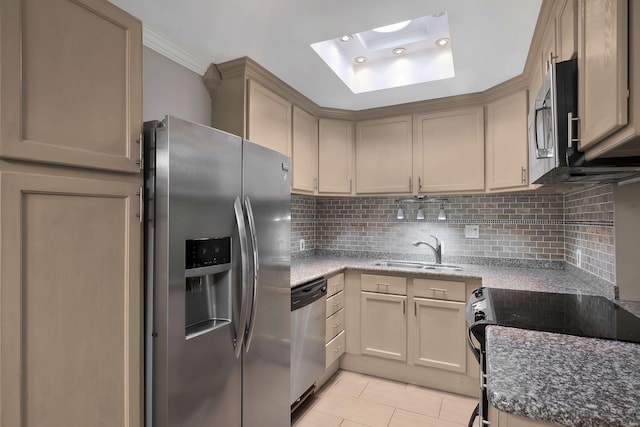 kitchen featuring appliances with stainless steel finishes, a sink, a skylight, decorative backsplash, and stone countertops