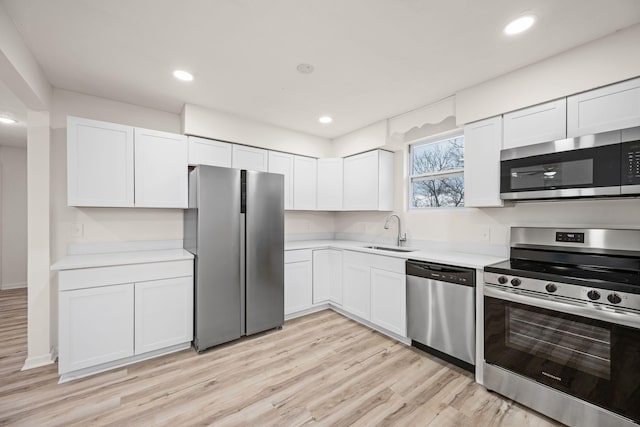 kitchen featuring appliances with stainless steel finishes, a sink, light countertops, light wood-style flooring, and white cabinets
