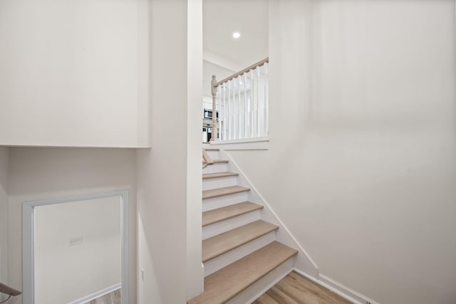 staircase featuring wood finished floors, baseboards, and recessed lighting