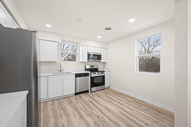kitchen with appliances with stainless steel finishes, a sink, light wood-type flooring, light countertops, and baseboards