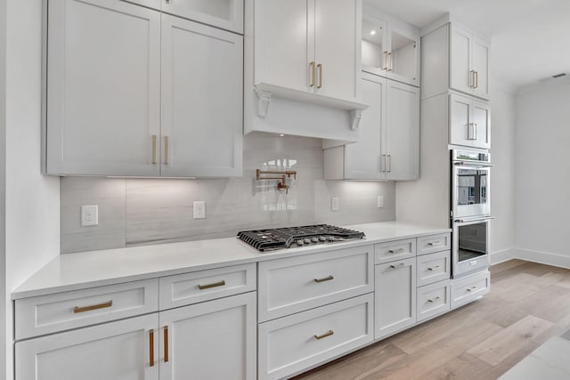 1018 Keeneland Dr, Gallatin, TN 37066 - kitchen featuring appliances with stainless steel finishes, decorative backsplash, light countertops, light wood finished floors, and glass insert cabinets